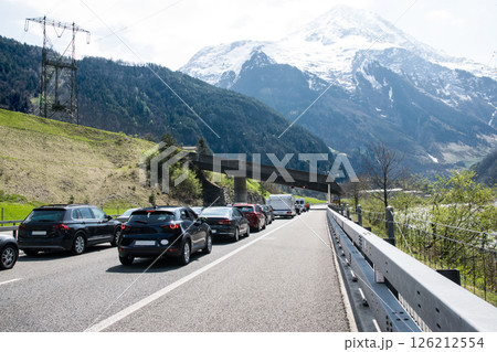 A lot of cars stay in traffic jam on the road near tunnel with mountains and forest in Switzerland. A lot of cars stay in traffic jam on the road near tunnel with mountains and forest in Switzerland. 126212554