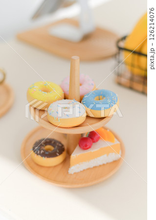 Close up view of colorful donuts with sprinkles on wooden stand featuring slice of cake creating delightful and tasty presentation in bright setting Close up view of colorful donuts with sprinkles on wooden stand featuring slice of cake creating delightful and tasty presentation in bright setting 126214076