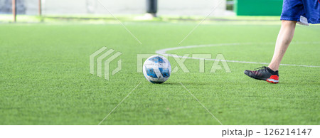 Soccer ball on green grass field with player wearing black cleats and blue shorts preparing to kick ball during game on sunny day Soccer ball on green grass field with player wearing black cleats and blue shorts preparing to kick ball during game on sunny day 126214147