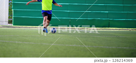 Soccer player in bright yellow jersey kicking ball on green artificial turf field during practice session with green padded wall in background Soccer player in bright yellow jersey kicking ball on green artificial turf field during practice session with green padded wall in background 126214369