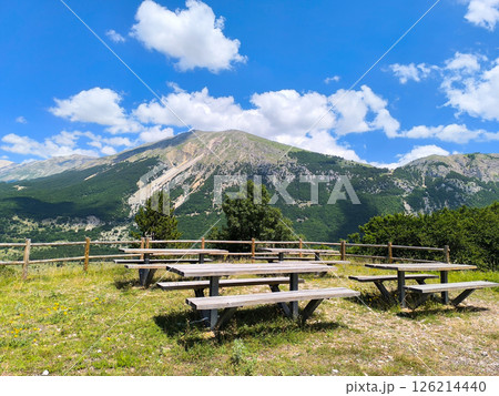 Scenic picnic area with wooden tables surrounded by breathtaking mountains under a clear blue sky 126214440