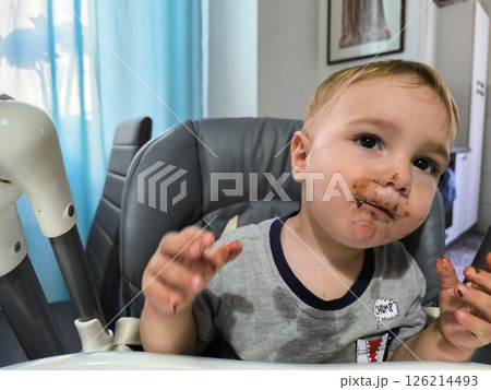 Little explorer enjoying a messy chocolate treat while seated in a cozy high chair on a sunny afternoon 126214493