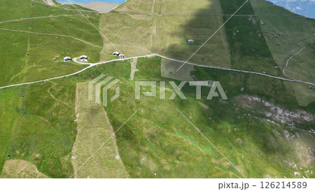 Expansive green valleys dotted with quaint cottages under a clear blue sky in the alpine region 126214589