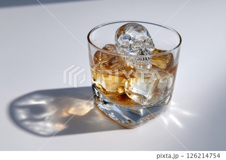 Glass of whiskey with ice cubes and skull shaped ice cube casts shadow on white surface, creating dramatic and intriguing scene 126214754