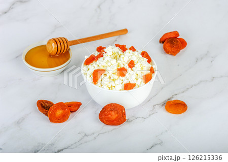 Fresh cottage cheese with dried apricots and honey in a white bowl and ingredients around the bowl. Fresh cottage cheese with dried apricots and honey in a white bowl and ingredients around the bowl. 126215336