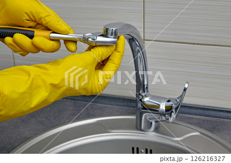 plumber in yellow rubber gloves repairing and servicing a water faucet in a kitchen plumber in yellow rubber gloves repairing and servicing a water faucet in a kitchen 126216327