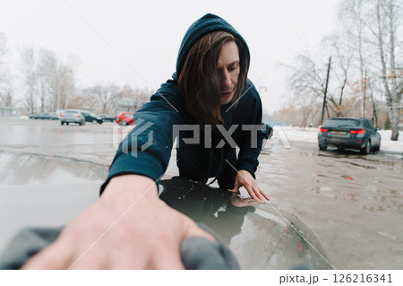 A person is focused on cleaning the hood of a car in a snowy parking lot. A person is focused on cleaning the hood of a car in a snowy parking lot. 126216341