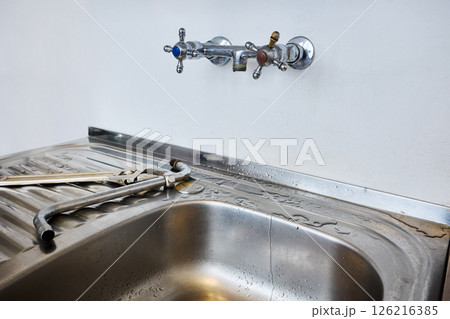 Stainless steel kitchen sink with detached faucet spout lying next to adjustable wrench and pipe wrench on wet draining surface after repair. Stainless steel kitchen sink with detached faucet spout lying next to adjustable wrench and pipe wrench on wet draining surface after repair. 126216385
