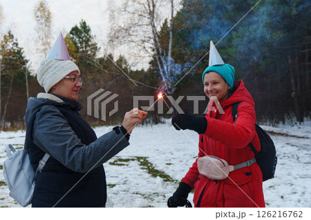 Two friends celebrating joyfully with sparklers in a snowy forest during winter festivities 126216762