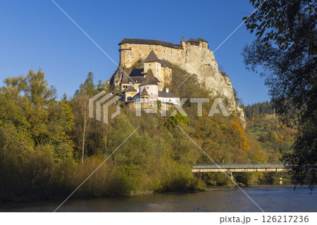 Oravsky Castle rising above Orava river and autumn foliage under blue sky Oravsky Castle rising above Orava river and autumn foliage under blue sky 126217236