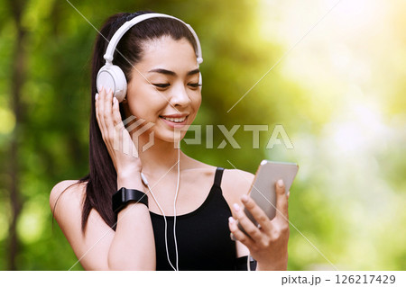 Online Music App. Cheerful Jogger Girl With Smartphone And Headphones Choosing Playlist For Running Outdoors Online Music App. Cheerful Jogger Girl With Smartphone And Headphones Choosing Playlist For Running Outdoors 126217429