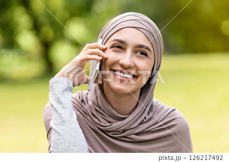 Happy girl in hijab talking with friend or lover on smartphone while resting at public park, copy space 126217492