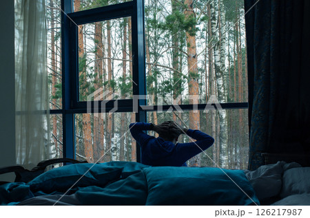 A depressed person by window. Dressed in blue, loneliness, blue atmosphere. coloritin commemoration of Blue Monday. World Mental Health Day. World Suicide Prevention Day 126217987