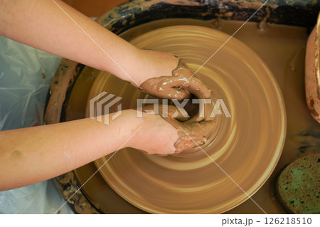 The potter's wheel. A close-up of the hands of a craftsman skillfully working with clay on a potter's wheel, giving it the shape of a clay product The potter's wheel. A close-up of the hands of a craftsman skillfully working with clay on a potter's wheel, giving it the shape of a clay product 126218510