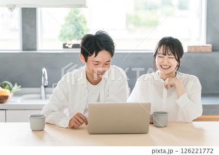 パソコンを見ながらリラックスして会話する仲良しの夫婦（ディンクス・カップル・くつろぐ） 126221772