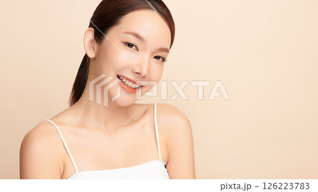 A beautiful young Asian woman with clean, fresh skin against a beige background. Skincare, facial treatment, cosmetology, beauty, and spa. An elegant portrait of an Asian woman. 126223783