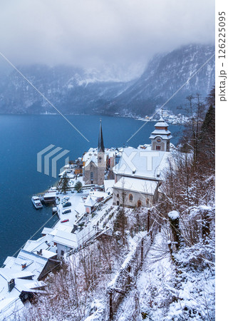 Hallstatt, Austria. Idyllic Alpine village snow-covered, serene lake, majestic mountains shrouded in a winter blizzard. Hallstatt, Austria. Idyllic Alpine village snow-covered, serene lake, majestic mountains shrouded in a winter blizzard. 126225095