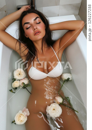 Beautiful woman in a bathtub with delicate flowers creating a calm atmosphere. Sexy young woman relaxing in a bath surrounded by flowers and serene lighting 126227288