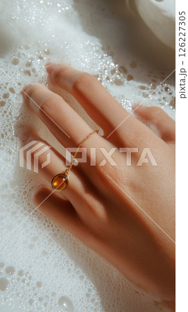A detailed artistic close-up of a hand adorned with gold jewelry amidst a bubble-laden surface, emphasizing elegance and softness with a luxurious feel. Jewelry, lifestyle, and beauty themes. 126227305