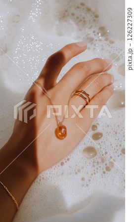 A detailed artistic close-up of a hand adorned with gold jewelry amidst a bubble-laden surface, emphasizing elegance and softness with a luxurious feel. Jewelry, lifestyle, and beauty themes. 126227309