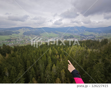 Female hand pointing into dark clouds above hilly landscape with forests 126227415