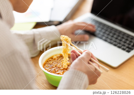 オフィスで仕事をしながらカップラーメンを食べるミドル男性 126228026