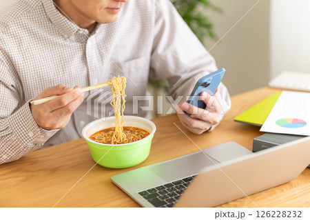 オフィスで仕事をしながらカップラーメンを食べるミドル男性 126228232