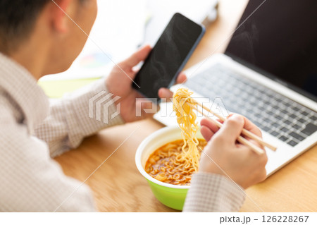 オフィスで仕事をしながらカップラーメンを食べるミドル男性 126228267