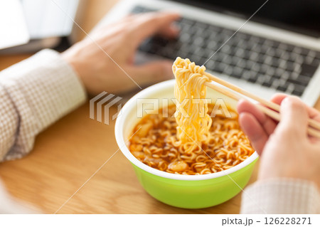 オフィスで仕事をしながらカップラーメンを食べるミドル男性 オフィスで仕事をしながらカップラーメンを食べるミドル男性 126228271