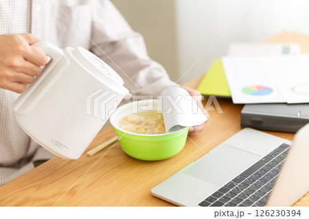 オフィスで仕事をしながらカップラーメンを食べるミドル男性 オフィスで仕事をしながらカップラーメンを食べるミドル男性 126230394