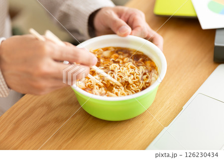 オフィスで仕事をしながらカップラーメンを食べるミドル男性 126230434