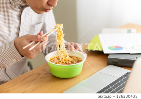 オフィスで仕事をしながらカップラーメンを食べるミドル男性 126230435