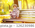 Little boy with yellow balloon is sitting in park at autumn background. 126230986