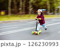 Little boy in cap is happily riding scooter at summer park background. 126230993