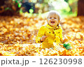 Little happy boy in yellow jacket is playing with leaves at golden autumn park background. 126230998
