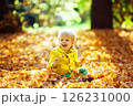 Little happy boy in yellow jacket is playing with leaves at golden autumn park background. 126231000