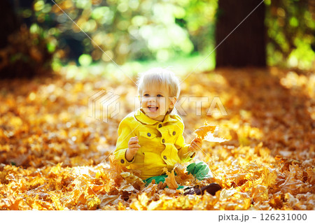 Little happy boy in yellow jacket is playing with leaves at golden autumn park background. 126231000