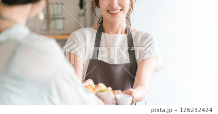 キッチン,カウンターから食事を手渡すエプロン姿のカフェ店員のアジア人女性 キッチン,カウンターから食事を手渡すエプロン姿のカフェ店員のアジア人女性 126232424