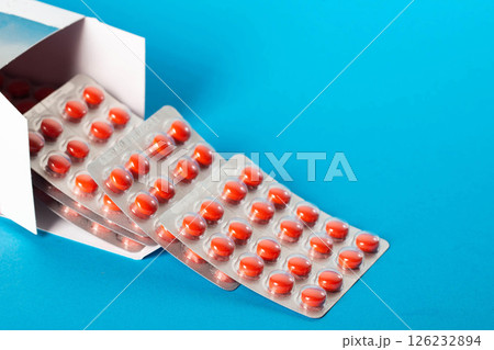 Blister pack of red pills on blue background. Concept of vitamins magnesium, minerals and calcium in pharmaceuticals. Copy space for text, close-up Blister pack of red pills on blue background. Concept of vitamins magnesium, minerals and calcium in pharmaceuticals. Copy space for text, close-up 126232894