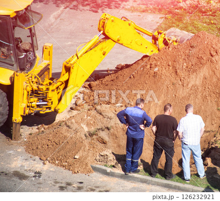 Workers stand near a pit with a loader with sand and emergency services in the background. Sewer leak repair, gas service, Close-up Workers stand near a pit with a loader with sand and emergency services in the background. Sewer leak repair, gas service, Close-up 126232921