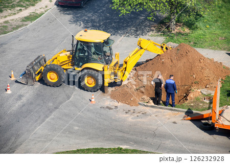A yellow excavator dug up a road to lay electrical cables, workers stand near the hole, industry. Copy space for text 126232928
