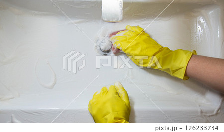 A girl washes and cleans the sink with a cleaning agent wearing yellow rubber gloves. Whitening and shine product, close-up. Copy space for text A girl washes and cleans the sink with a cleaning agent wearing yellow rubber gloves. Whitening and shine product, close-up. Copy space for text 126233734