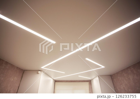 Modern designer stretch ceiling with illuminated LED lines in the room, backlighting Modern designer stretch ceiling with illuminated LED lines in the room, backlighting 126233755