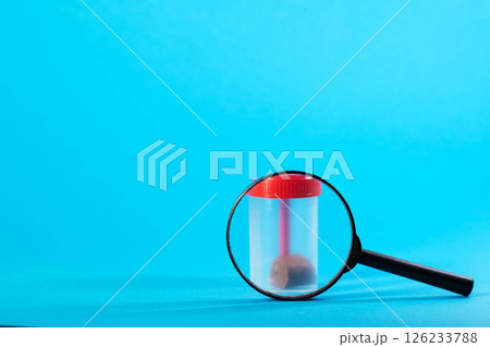 Magnifying glass with stool analysis container on a blue background. Concept of stool tests calprotectin and protozoan parasites. Copy space for text, cologram 126233788