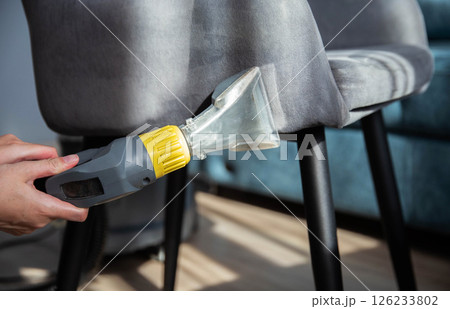 A girl s hand with a washing vacuum cleaner cleans the gray upholstery of a fabric chair in the apartment from dirt. Cleaning services, upholstered furniture cleaning 126233802