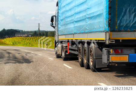 A truck with a semi-trailer transports cargo along the road in summer. The concept of a freight exchange and freight forwarders and truckers. Copy space for text, brand 126233825