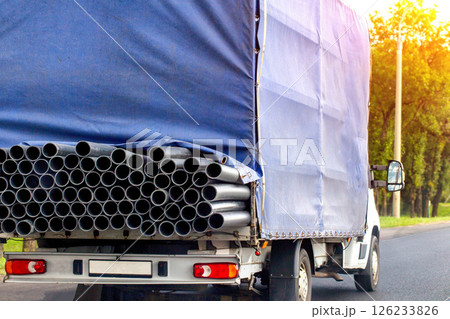 Transportation of metal pipes in a truck on a road in summer against the backdrop of the sun, industry. Transport company that provides metal transportation services, close-up 126233826