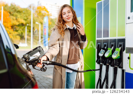 Beautiful woman filling car with gasoline at gas station. Online pay. Woman using app on phone. 126234143