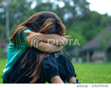 Unhappy sad little girl sitting alone hugging her knees in the park. 126234192