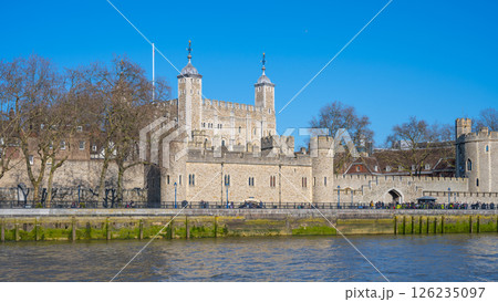 Tower Wharf offers a stunning view of the historical Tower of London under clear blue skies. Visitors admire the ancient architecture by the River Thames, enjoying a pleasant day outdoors. 126235097